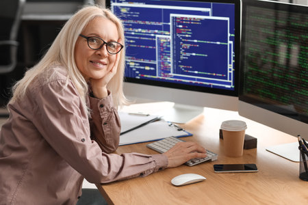 Mature female programmer working with computer at table in officeの写真素材