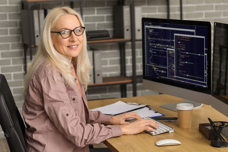 Mature female programmer working with computer at table in officeの写真素材