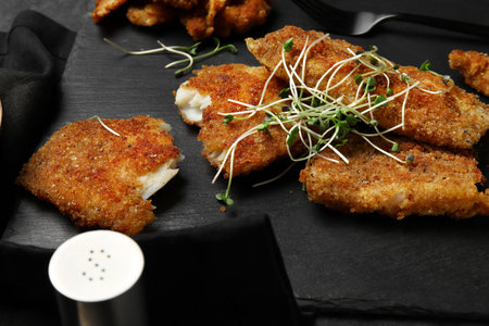 Slate board of tasty fried codfish on dark background, closeup
