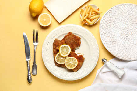 Plate of tasty fried codfish with lemon and french fries on yellow backgroundの写真素材