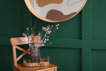 Vase with blooming branches on stool near mirror in roomの写真素材
