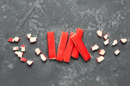 Tasty cut and whole crab sticks on green background