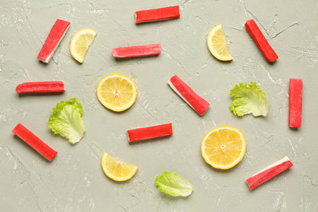 Tasty crab sticks, slices of lemon and lettuce on light background