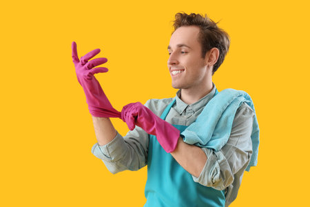 Young man putting on rubber gloves against yellow backgroundの写真素材