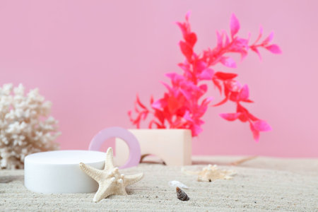 Decorative plaster podiums, coral, seaweed and starfish in sand on pink backgroundの写真素材