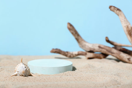 Decorative plaster podium, seashell and tree branch in sand on blue backgroundの写真素材