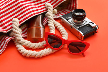 Photo camera, sunglasses, bottle of sunscreen and bag on red backgroundの写真素材