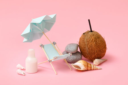 Miniature deck chair, coconut with straw, bottle of sunscreen and seashells on pink backgroundの写真素材