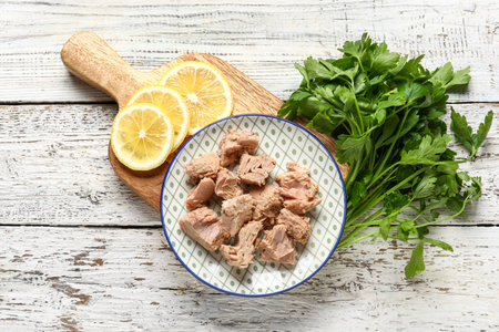 Plate with delicious canned tuna, lemons and parsley on white wooden tableの写真素材