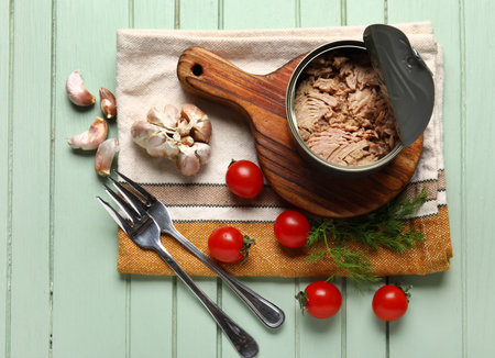 Composition with opened tin can of tuna, tomatoes, garlic and forks on green wooden tableの写真素材
