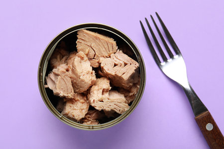 Opened tin can with delicious tuna and fork on lilac backgroundの写真素材