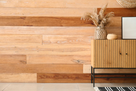 Chest of drawers with blank frame, basket and pampas grass near wooden wall in roomの写真素材