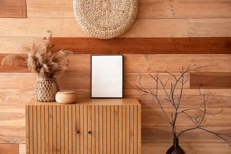 Chest of drawers with blank frame, basket and pampas grass near wooden wallの写真素材