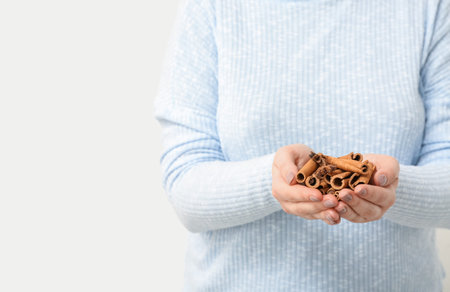 Woman with aromatic cinnamon sticks on white background, closeup