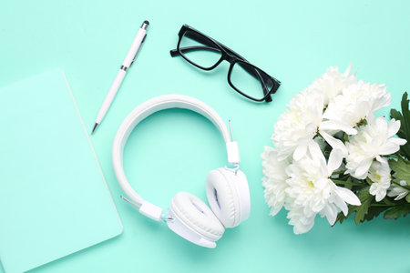 Modern headphones, eyeglasses, notebook, pen and chrysanthemum flowers on color backgroundの写真素材