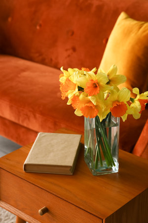 Vase with narcissus flowers and book on end table in living roomの写真素材