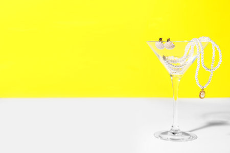 Glass with pearl jewelry on table against yellow backgroundの写真素材