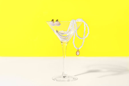 Glass with pearl jewelry on table against yellow backgroundの写真素材