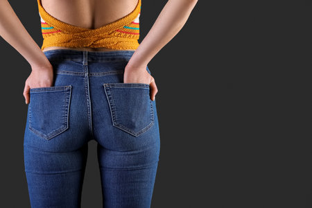 Young woman in skinny jeans on dark background, back viewの写真素材