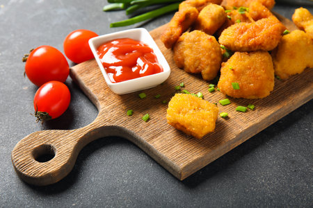 Board with delicious nuggets, ketchup and vegetables on black tableの写真素材