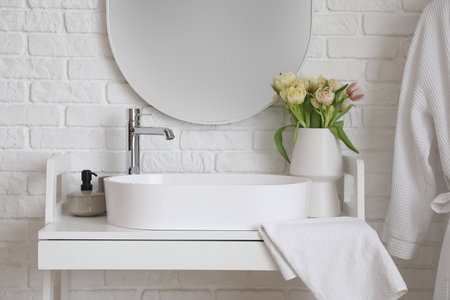 Mirror hanging on white brick wall near sink and vase with tulip flowersの写真素材