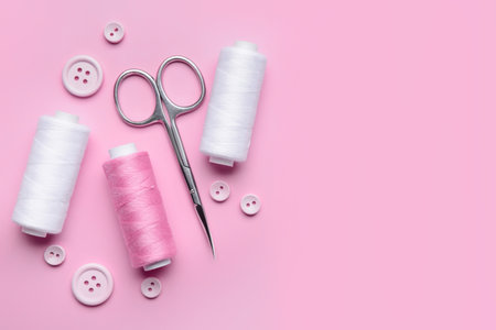 Composition with thread spools, buttons and scissors on pink backgroundの写真素材