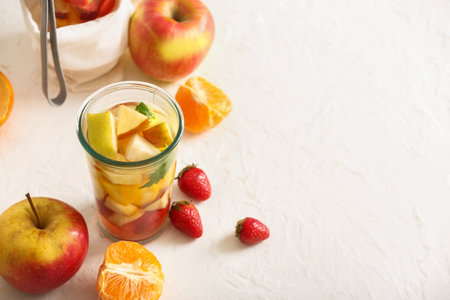 Glass of infused water with different sliced fruits on white tableの写真素材