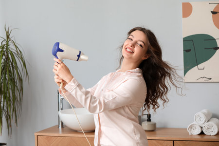 Pretty young woman with hair dryer in bathroomの写真素材