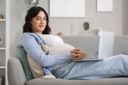 Young pregnant woman working with laptop on sofa at homeの写真素材