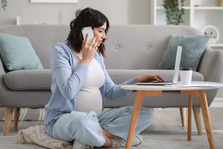 Working pregnant woman talking by mobile phone at homeの写真素材