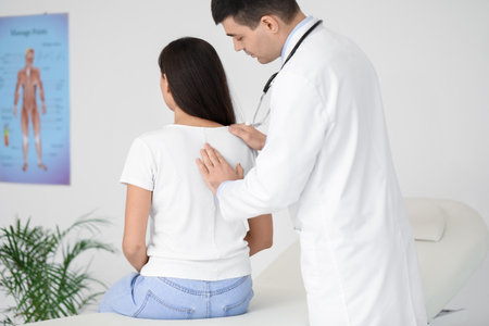 Male doctor checking posture of young woman in clinicの写真素材