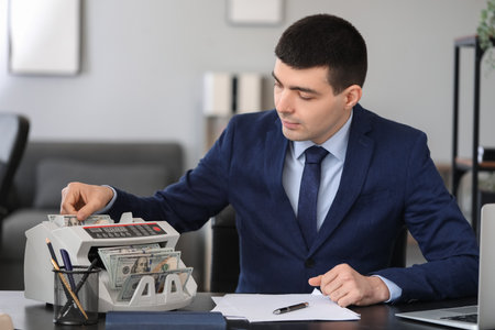 Male bank manager working with cash counting machine in officeの写真素材