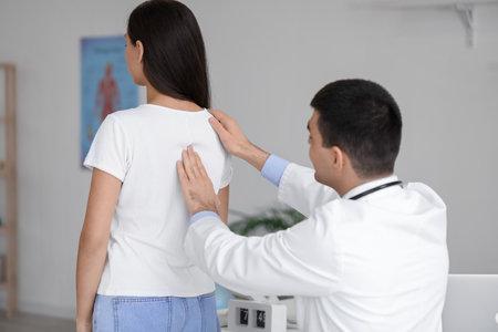 Male doctor checking posture of young woman in clinicの写真素材