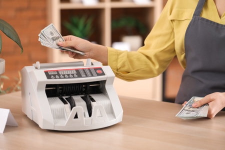 Female cashier using cash counting machine in flower shop, closeup