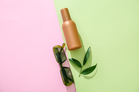 Bottle of sunscreen cream with sunglasses and tree branch on color backgroundの写真素材