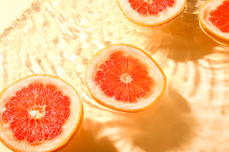 Slices of fresh grapefruit in water on yellow backgroundの写真素材