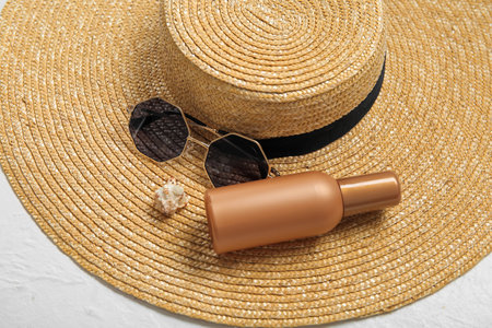 Bottle of sunscreen cream, wicker hat, seashell and sunglasses on light background, closeupの写真素材