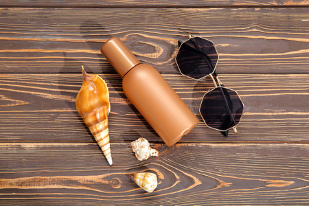 Bottle of sunscreen cream, sunglasses and seashells on wooden background