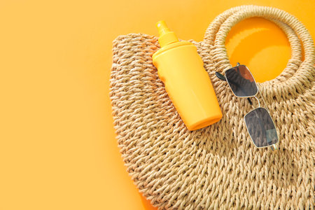 Bottle of sunscreen cream with sunglasses and wicker bag on orange backgroundの写真素材
