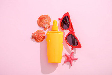 Bottle of sunscreen cream with sunglasses and seashells on pink background