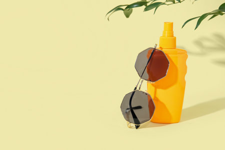 Bottle of sunscreen cream with sunglasses and tree branch on pale yellow backgroundの写真素材
