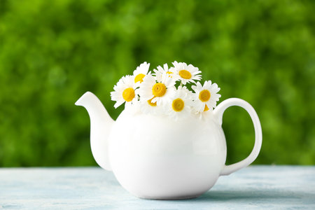 Teapot with beautiful chamomile flowers on blue table outdoorsの写真素材