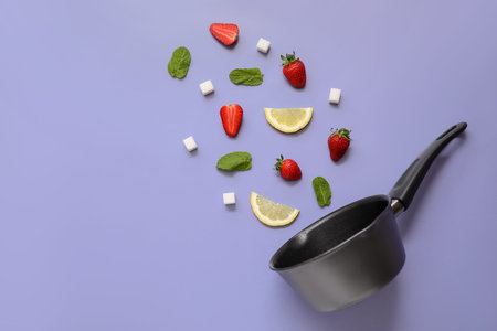 Saucepan and ingredients for preparing strawberry compote on purple background