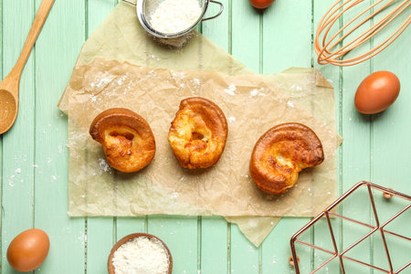 Tasty Yorkshire pudding and ingredients on green wooden background