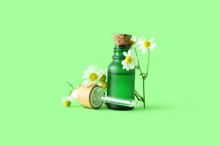Bottle of essential oil and fresh chamomile flowers on green backgroundの写真素材