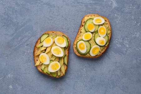 Tasty toasts with quail eggs, avocado and cucumber on blue background