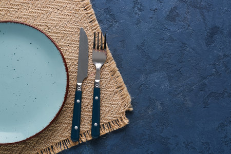Silver knife with fork, plate and kitchen mat on blue grunge backgroundの写真素材