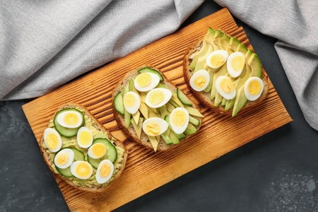 Tasty toasts with quail eggs, avocado and cucumber on dark grunge backgroundの写真素材
