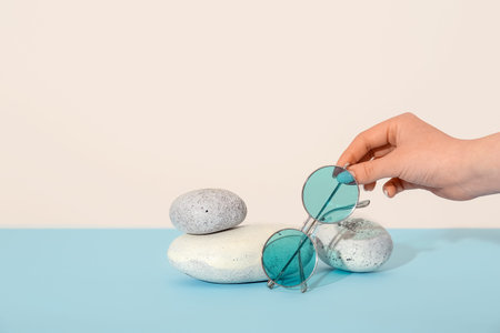 Female hand and stones with stylish sunglasses on blue tableの写真素材