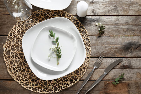 Wicker mat with stylish table setting and candle on brown wooden background